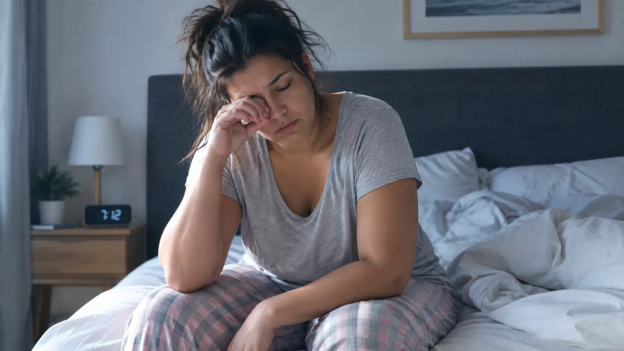 Femme fatiguée assise sur son lit au réveil, se frottant les yeux, illustrant la fatigue liée à l'apnée du sommeil silencieuse.